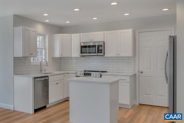 kitchen featuring stainless steel appliances, light wood-style flooring, white cabinetry, a kitchen island, and a sink