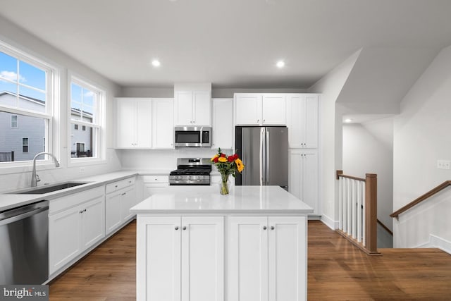 kitchen featuring dark wood-type flooring, a center island, stainless steel appliances, white cabinetry, and a sink