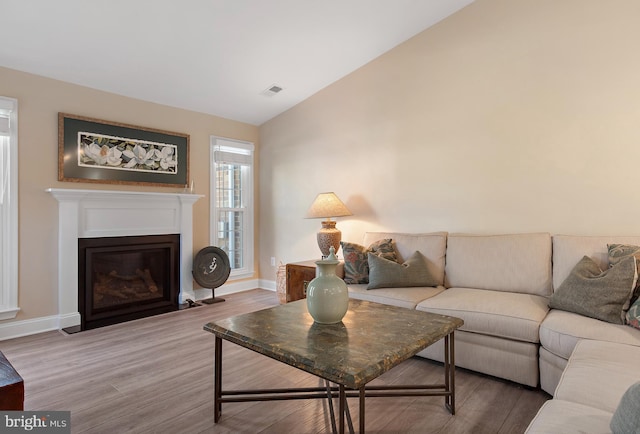 living area with visible vents, baseboards, a fireplace with flush hearth, wood finished floors, and vaulted ceiling