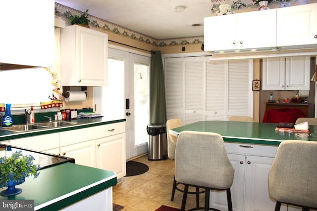 kitchen with light tile patterned floors, a breakfast bar, a sink, white cabinetry, and dark countertops