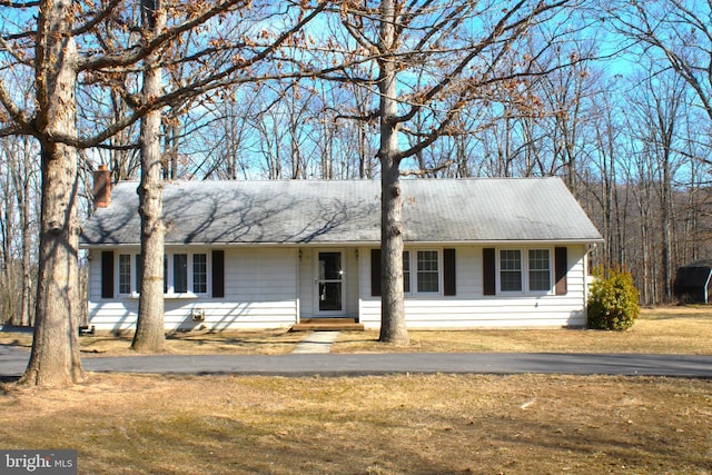 ranch-style house featuring a shingled roof, a chimney, and a front lawn