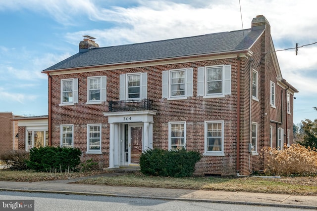 colonial house featuring brick siding, a chimney, and roof with shingles