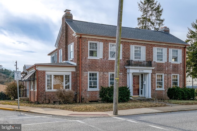 view of front of house with brick siding, a chimney, and a shingled roof