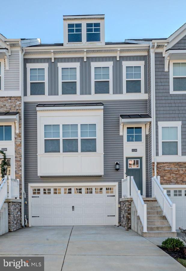 townhome / multi-family property featuring driveway, stone siding, board and batten siding, and an attached garage