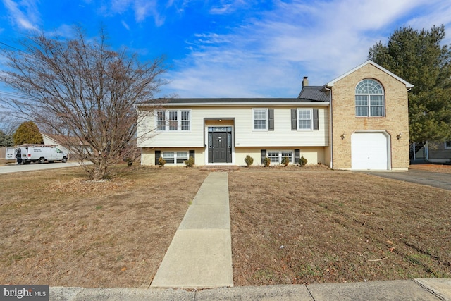 raised ranch with driveway, a front lawn, a chimney, and an attached garage