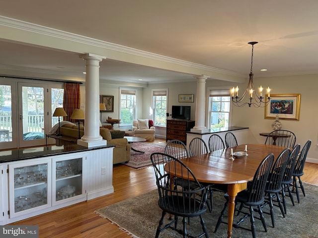 dining space featuring crown molding, light wood-style floors, and ornate columns