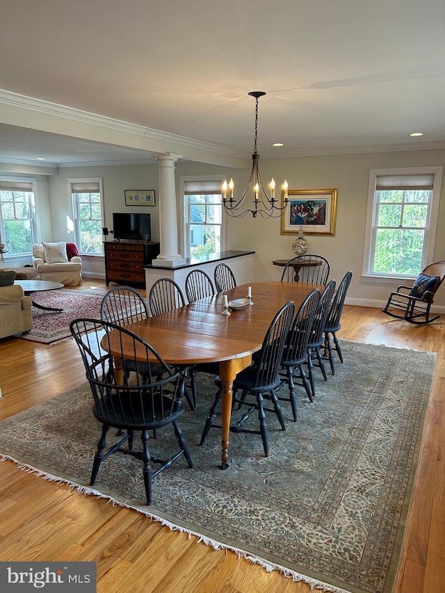 dining space with decorative columns, wood finished floors, and ornamental molding