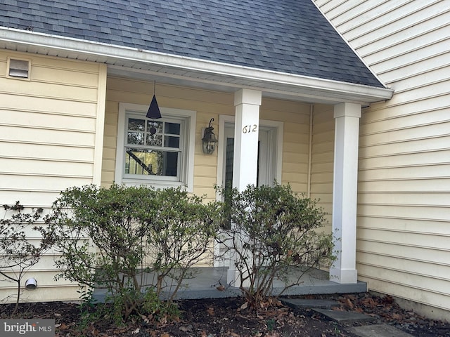 entrance to property featuring a porch and roof with shingles