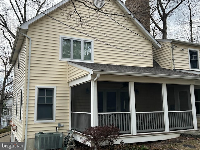 view of side of home with roof with shingles, central AC, a chimney, and a sunroom