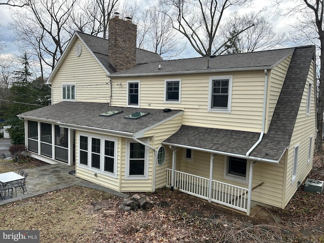 back of house featuring covered porch, roof with shingles, a sunroom, a chimney, and a patio area