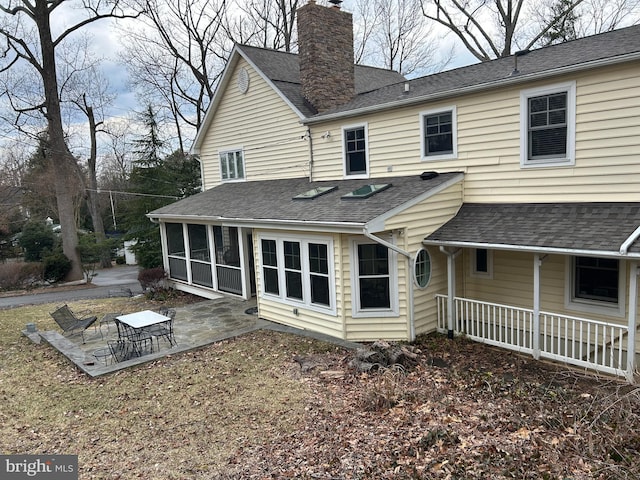 back of house with a shingled roof, a patio, a sunroom, and a chimney