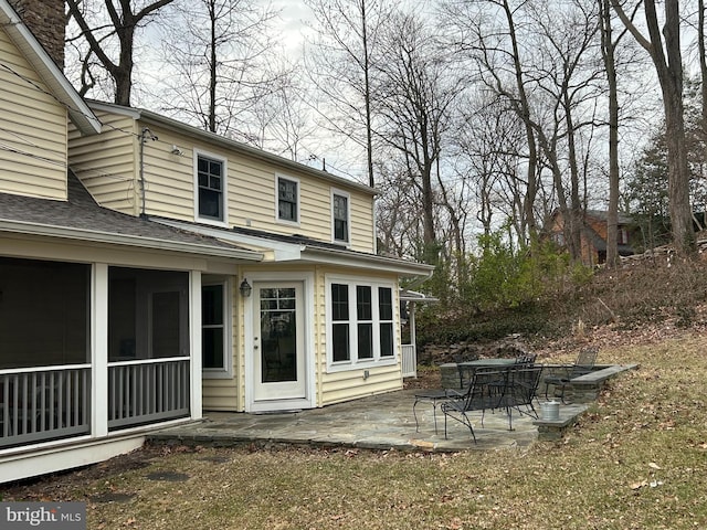 rear view of house with a patio, a sunroom, and roof with shingles