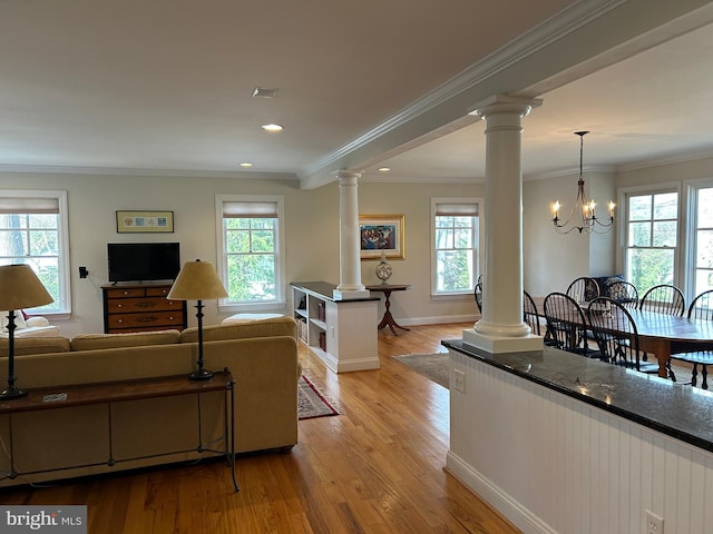 living area featuring a notable chandelier, ornamental molding, light wood finished floors, decorative columns, and baseboards