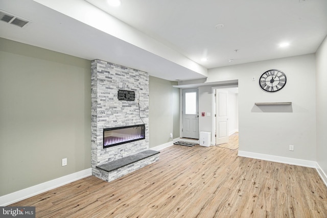 unfurnished living room with a stone fireplace, recessed lighting, wood finished floors, visible vents, and baseboards