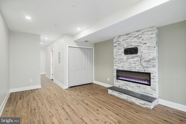 unfurnished living room with recessed lighting, a stone fireplace, wood finished floors, electric panel, and baseboards