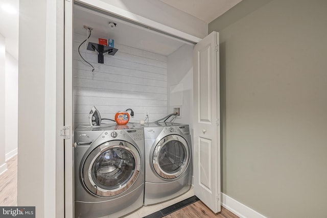 laundry area featuring wooden walls, separate washer and dryer, wood finished floors, laundry area, and baseboards