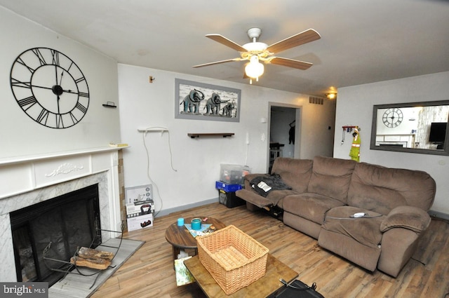 living area with a premium fireplace, wood finished floors, a ceiling fan, visible vents, and baseboards