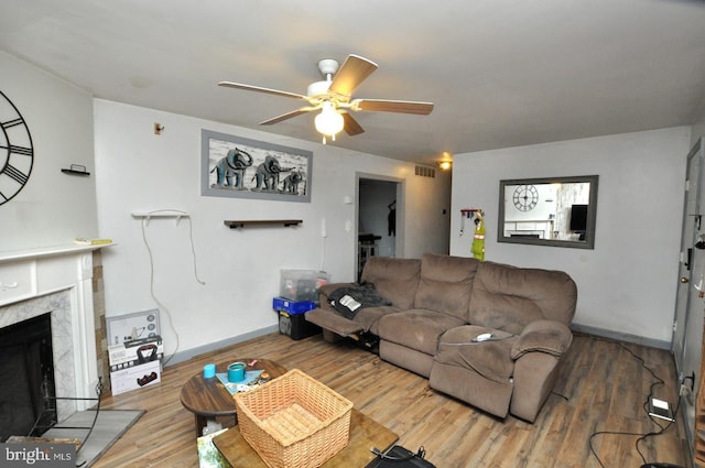 living room featuring visible vents, baseboards, a ceiling fan, wood finished floors, and a high end fireplace