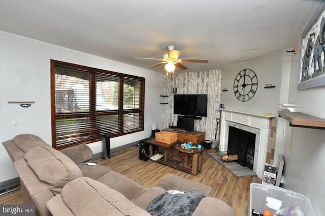 living area featuring visible vents, ceiling fan, a premium fireplace, and wood finished floors