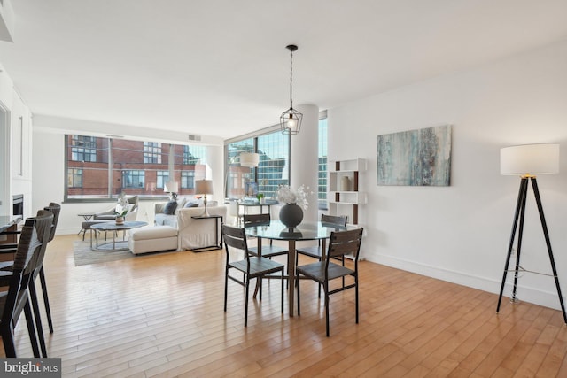 dining room featuring floor to ceiling windows, a fireplace, light wood-style flooring, and baseboards