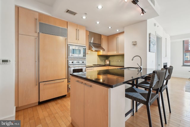 kitchen with built in appliances, under cabinet range hood, a breakfast bar, a sink, and visible vents