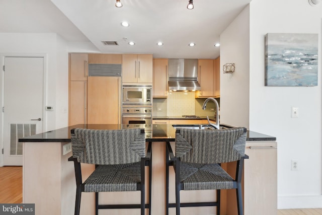 kitchen featuring visible vents, light wood-style floors, light brown cabinets, built in appliances, and a kitchen breakfast bar