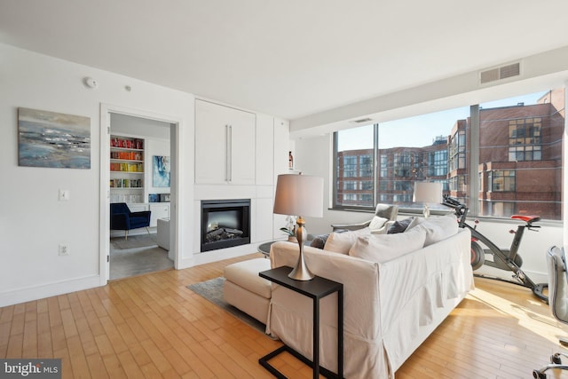 living room featuring light wood-style floors, visible vents, a fireplace, and built in features