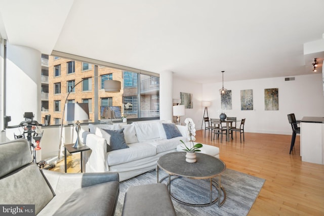 living area featuring light wood-style floors, baseboards, floor to ceiling windows, and visible vents