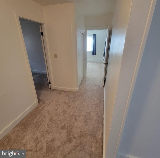 corridor with baseboards and light colored carpet