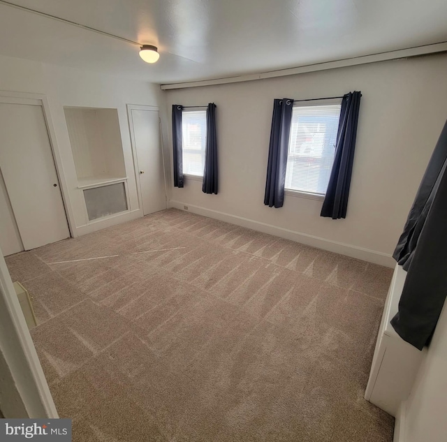 unfurnished bedroom featuring multiple closets, light carpet, and baseboards