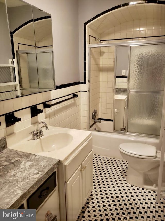 full bathroom featuring toilet, bath / shower combo with glass door, vanity, tile walls, and tile patterned floors