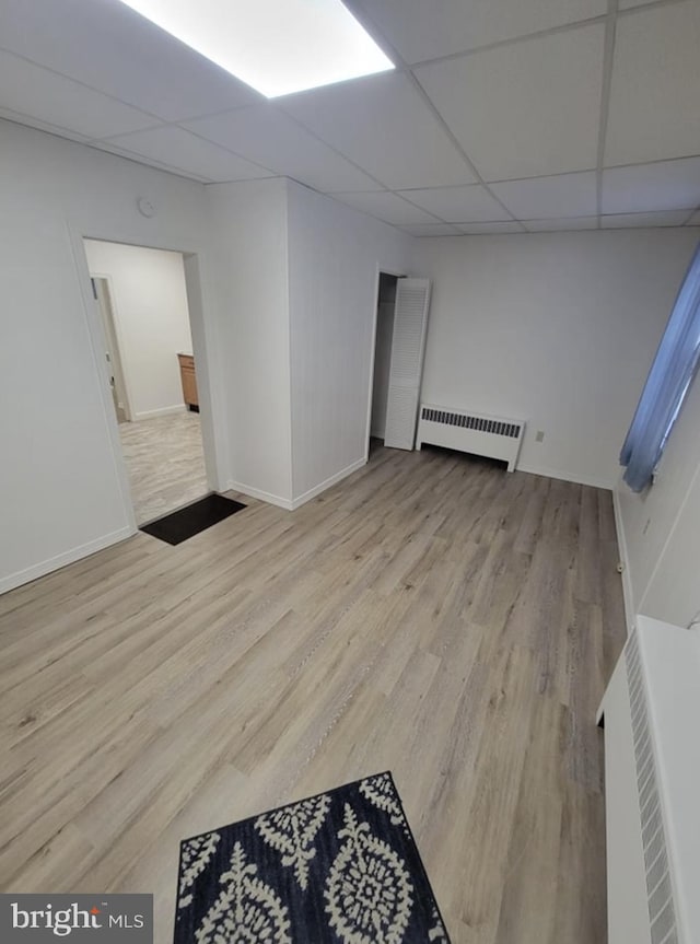 unfurnished room featuring radiator heating unit, baseboards, a drop ceiling, and wood finished floors