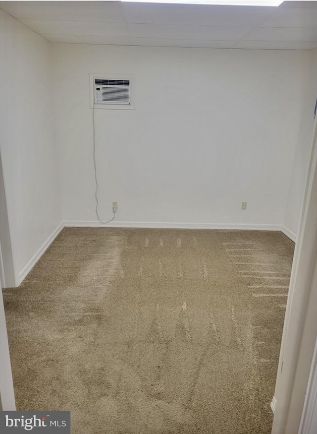 carpeted spare room with baseboards, a drop ceiling, and an AC wall unit