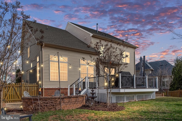 back of house featuring fence, roof with shingles, a yard, a deck, and brick siding