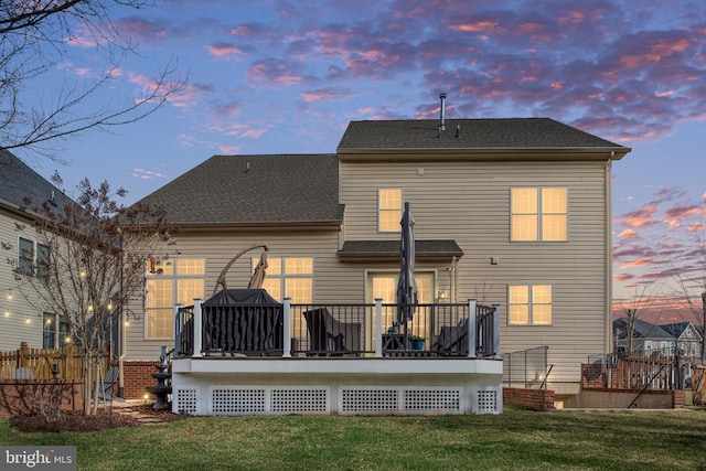 rear view of house with a shingled roof, a wooden deck, a yard, and fence