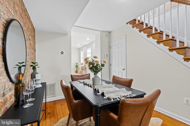 dining area featuring brick wall, visible vents, baseboards, stairs, and wood-type flooring