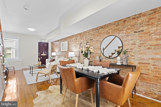 dining space with wood-type flooring, baseboards, brick wall, and stairs