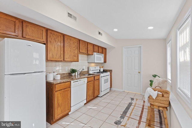 kitchen featuring brown cabinets, light tile patterned floors, visible vents, decorative backsplash, and white appliances