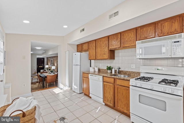 kitchen featuring white appliances, visible vents, decorative backsplash, brown cabinetry, and a sink