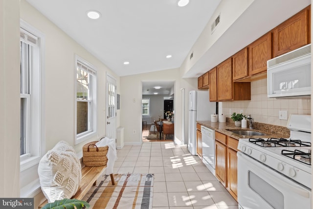 kitchen featuring light tile patterned floors, white appliances, a sink, decorative backsplash, and brown cabinets