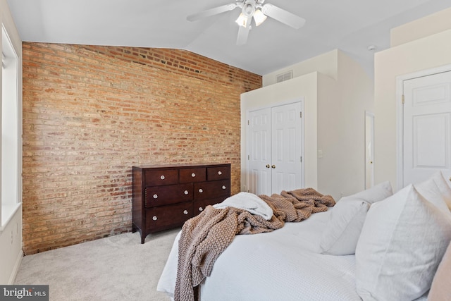 carpeted bedroom with visible vents, lofted ceiling, brick wall, ceiling fan, and a closet