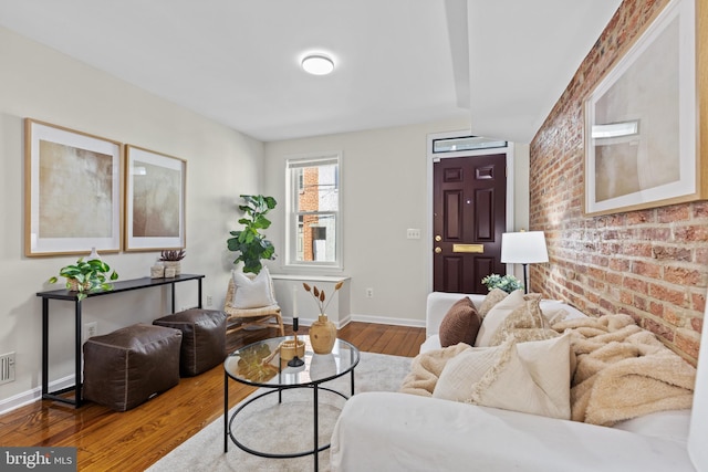 living area featuring brick wall, wood-type flooring, visible vents, and baseboards