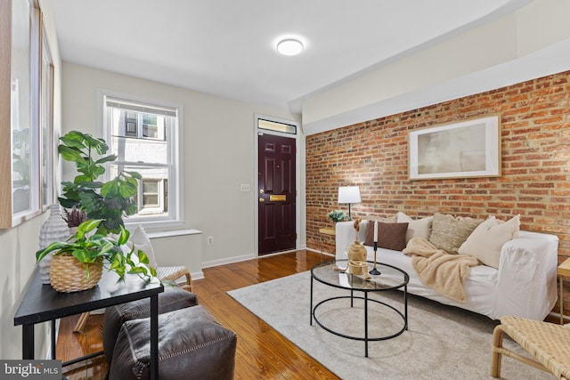 living room with baseboards, brick wall, and wood finished floors