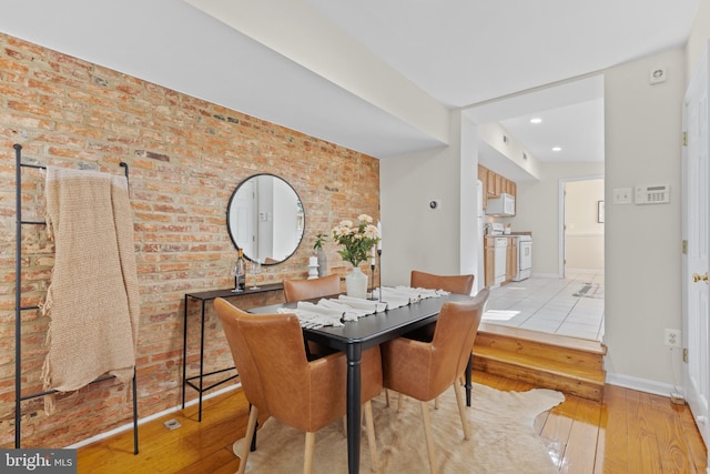 dining room with brick wall, wood-type flooring, and baseboards