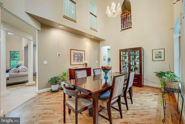 dining space featuring a chandelier, baseboards, a towering ceiling, and light wood-style floors