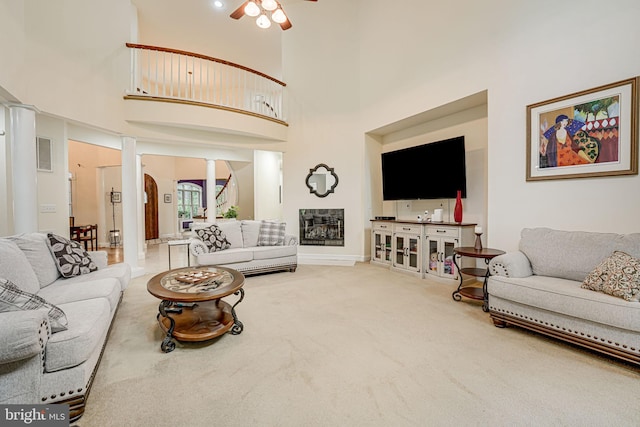 carpeted living room featuring a fireplace, visible vents, a towering ceiling, a ceiling fan, and ornate columns