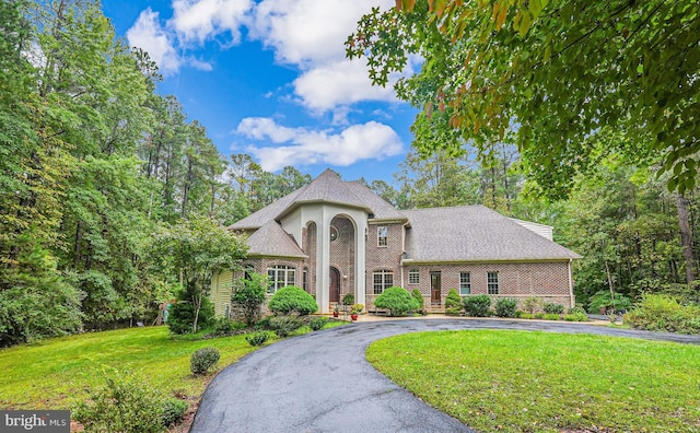 neoclassical home featuring aphalt driveway, brick siding, a front lawn, and roof with shingles