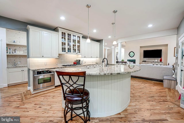 kitchen featuring light stone counters, oven, a breakfast bar, white cabinetry, and light wood finished floors