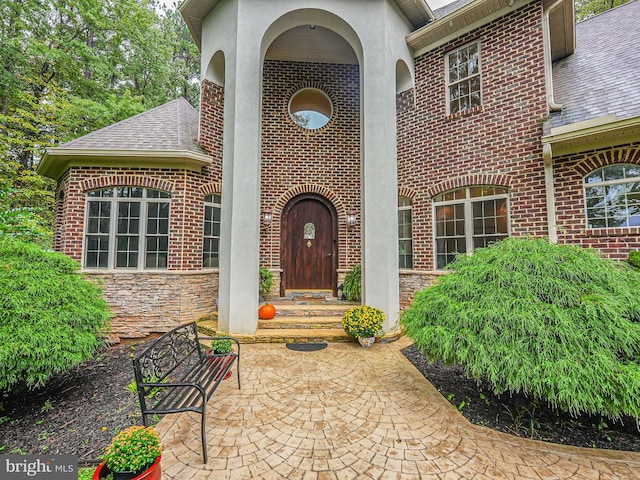 view of exterior entry featuring a shingled roof, stone siding, brick siding, and stucco siding