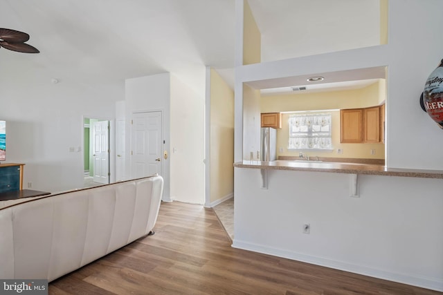 kitchen with a peninsula, light wood-style flooring, a kitchen bar, and freestanding refrigerator